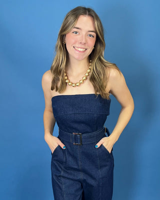 A woman modeling a dark blue denim strapless jumpsuit with wide legs and a matching belt
