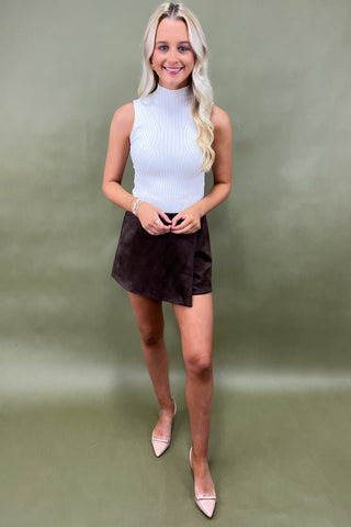 Woman wearing a white sleeveless top and brown skirt against a green background