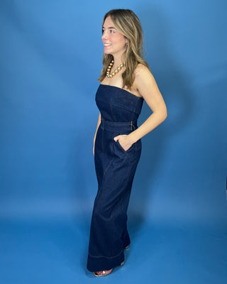 A woman modeling a dark blue denim strapless jumpsuit with wide legs and a matching belt
