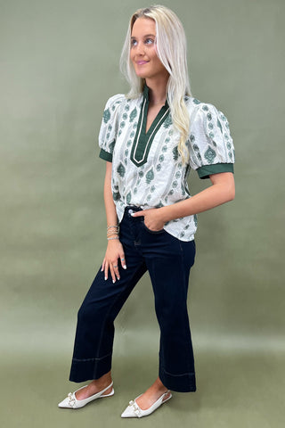 Woman wearing a patterned blouse and dark jeans against a plain background