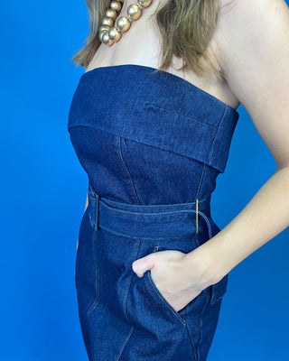 A woman modeling a dark blue denim strapless jumpsuit with wide legs and a matching belt