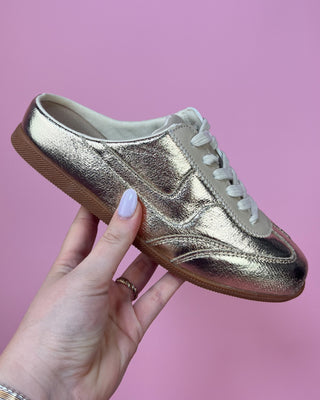 Metallic gold lace-up sneakers with a shiny textured finish, cream accents, white laces, and gum rubber soles. Stylish low-top fashion sneakers that combine sporty comfort with eye-catching metallic shine for casual everyday wear.