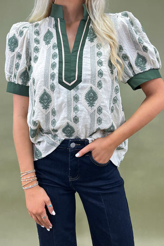 Woman wearing a patterned blouse and dark jeans against a plain background