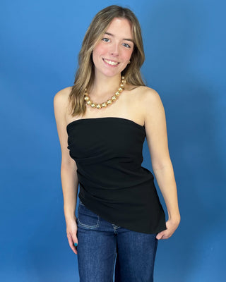 A woman modeling a black strapless ruched tube top with blue jeans and a gold beaded necklace