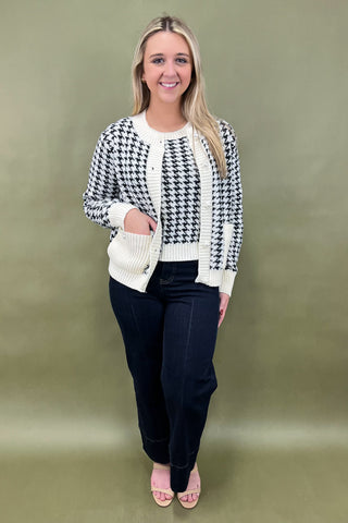 Woman wearing a black and white patterned cardigan over a white shirt with black pants on a green background