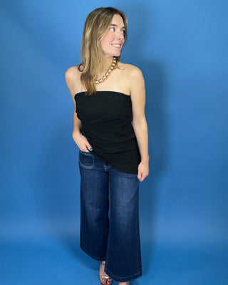 A woman modeling a black strapless tube top with dark wide-leg jeans