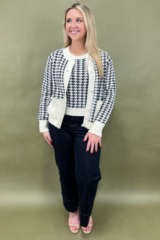Woman wearing a black and white checkered cardigan over a white top with black pants on a green background