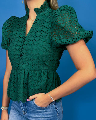 A woman wearing a dark green eyelet lace blouse with puff sleeves and a ruffled high neckline
