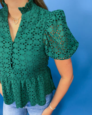 A woman wearing a green eyelet lace blouse with puff sleeves and a scalloped peplum hem, paired with light blue jeans