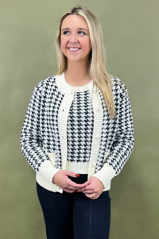 Woman wearing a black and white patterned cardigan against a green background