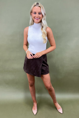 Woman wearing a white sleeveless top and brown skirt against a green background
