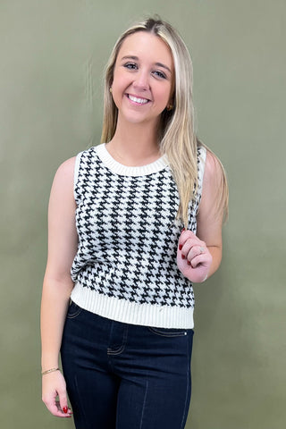 Woman wearing a black and white houndstooth patterned sleeveless top against a plain background
