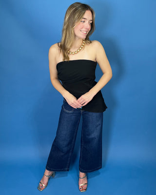 A woman modeling a black strapless bandeau top with wide-leg blue jeans and a chunky gold necklace