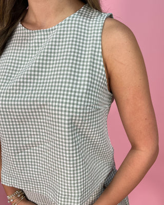 Person wearing a green and white checkered sleeveless top against a pink background