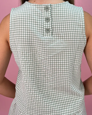 Green and white checkered sleeveless top worn by a person on a pink background