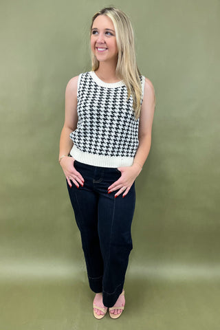 Woman wearing a black and white checkered sleeveless top and dark pants against a green background