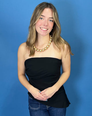 A smiling young woman with blonde hairwearing a black strapless tube top, blue jeans