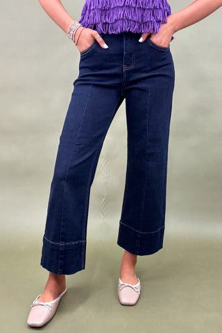 Person wearing dark blue wide-leg jeans and a purple top on a plain background