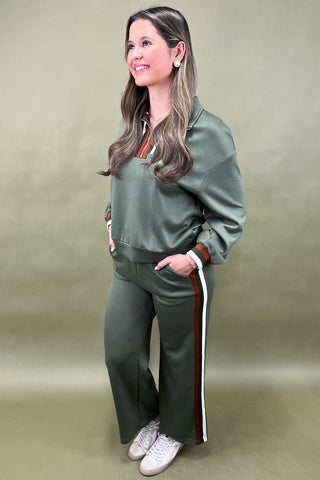 Woman wearing a green tracksuit with white and red stripes on a beige background