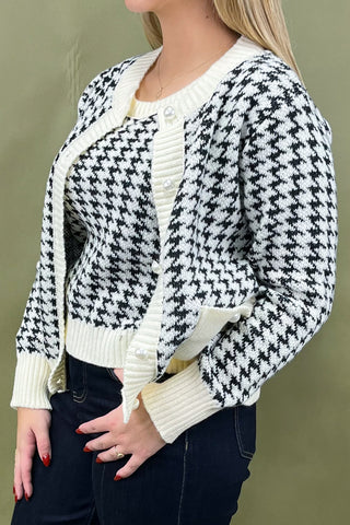Person wearing a black and white houndstooth patterned cardigan over a white shirt on a green background