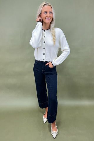 White button-front cardigan with black trim details styled with dark wide leg cropped jeans and white pointed loafers.