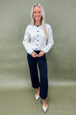 White button-front cardigan with black trim details styled with dark wide leg cropped jeans and white pointed loafers.