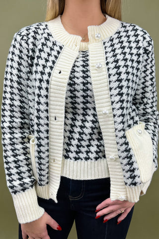 Black and white houndstooth patterned cardigan worn by a person on a green background