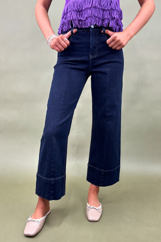 Person wearing dark blue wide-leg jeans and a purple top on a plain background