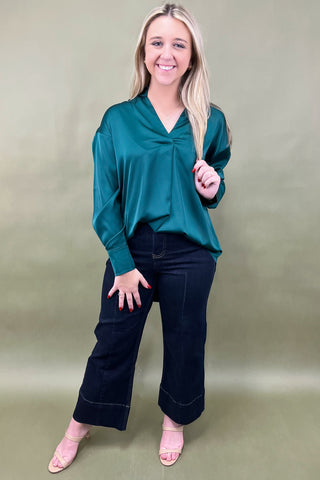 Woman wearing a teal top and black pants against a plain background