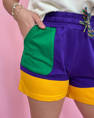 Colorful shorts with green, purple, and yellow sections on a pink background