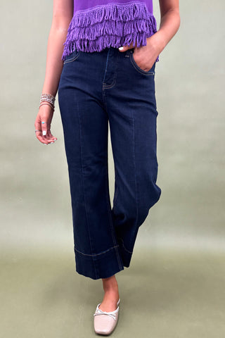 Person wearing a purple top with fringe and dark blue wide-leg pants on a plain background