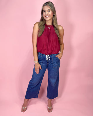 Woman wearing a red top and blue jeans against a pink background