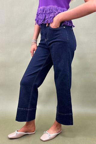 Person wearing navy blue pants and a purple top with fringe on a plain background