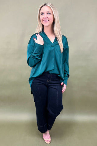 Woman wearing a teal blouse and black pants against a plain background