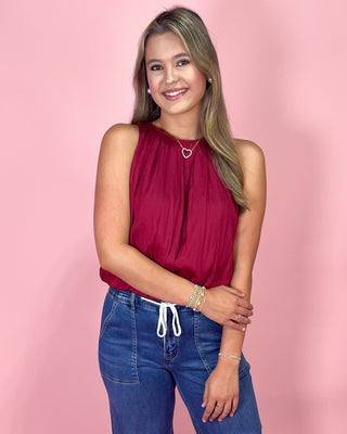 Woman wearing a red sleeveless top and blue jeans against a pink background