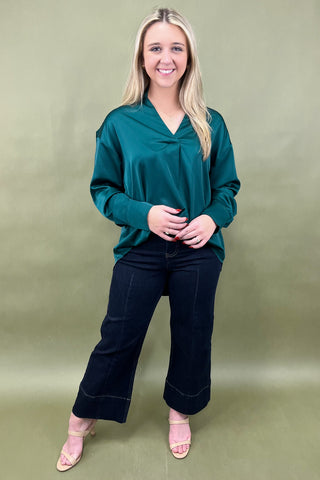 Woman wearing a teal top and black pants against a green background