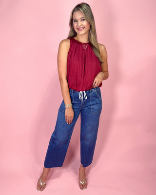 Woman wearing a red top and blue jeans against a pink background