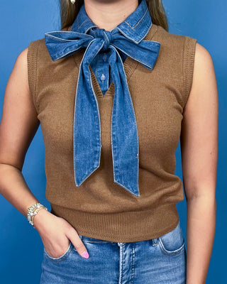 A person wearing a brown ribbed knit sleeveless sweater vest with a wide blue denim collar tied in a large bow at the neckline