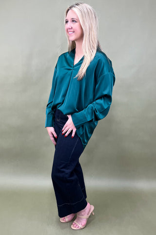 Woman wearing a teal top and dark pants against a plain background