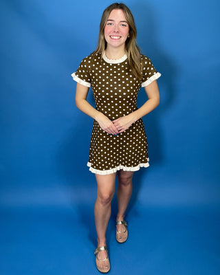 A young woman modeling a brown short-sleeve mini dress with white polka dots and white ruffle trim