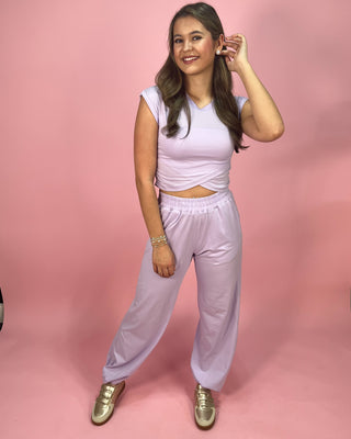 Woman wearing a light purple outfit with gold shoes on a pink background