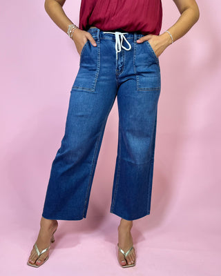 Person wearing blue wide-leg jeans and a red top on a pink background