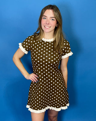 A young woman modeling a brown short-sleeve dress with white polka dots and white ruffled trim
