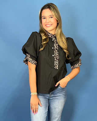 A woman modeling a black puff-sleeve blouse with leopard-print trim on the collar and cuffs, paired with light-wash blue jeans