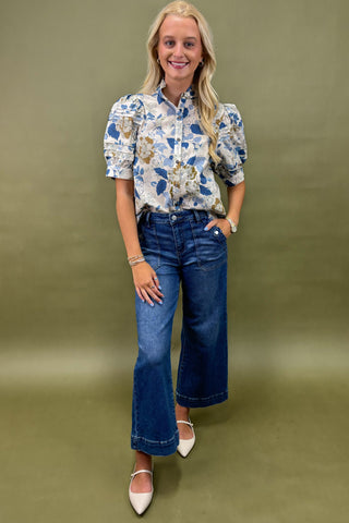 Woman wearing a floral blouse and blue jeans against a green background