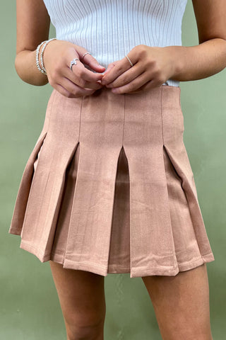 Person wearing a light blue top and pink pleated skirt against a green background