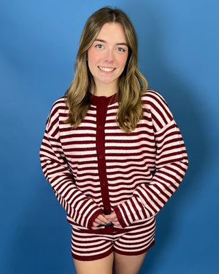 A young woman with blonde hair smiling, wearing a matching red and white striped knit cardigan and shorts set