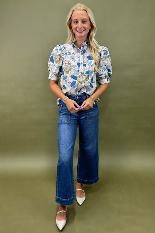Woman wearing a floral blouse and blue jeans against a green background