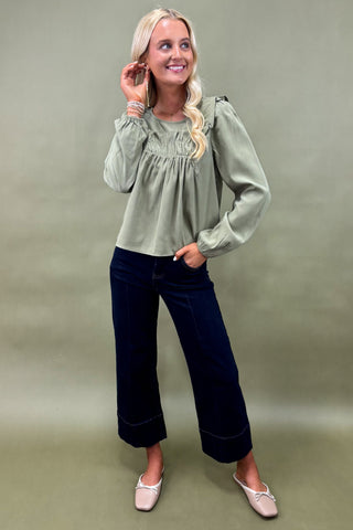 Woman wearing a green blouse and navy pants against a green background