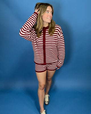 A woman modeling a matching two-piece loungewear set consisting of a long-sleeve cardigan and shorts, featuring a red and white horizontal stripe pattern with a solid red center placket